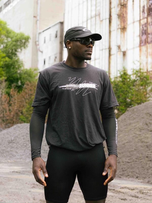 Man wearing a dark long-sleeve shirt with a logo and text, standing in an urban setting.